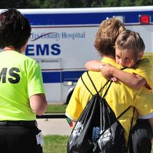 A child hugs an adult in front of an ambulance